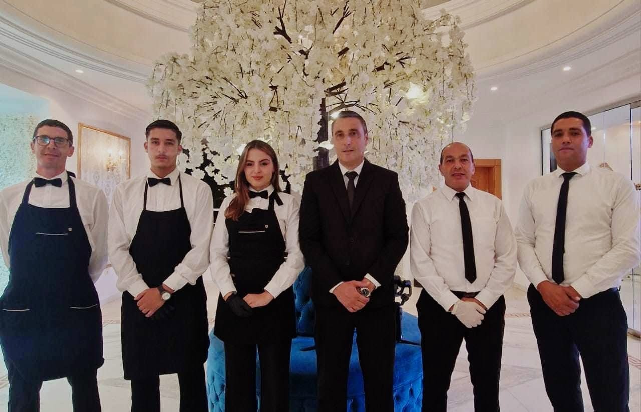 L’équipe de service au complet, en tenue de réception, devant un décor floral blanc